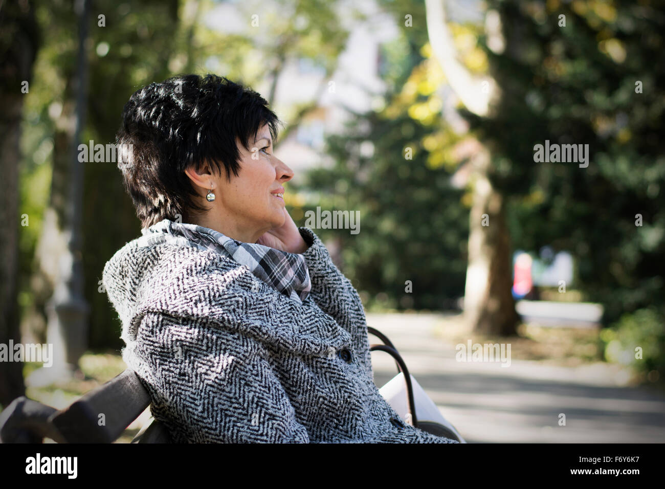 Beautiful middleaged woman with short dark haircut using device in park Stock Photo