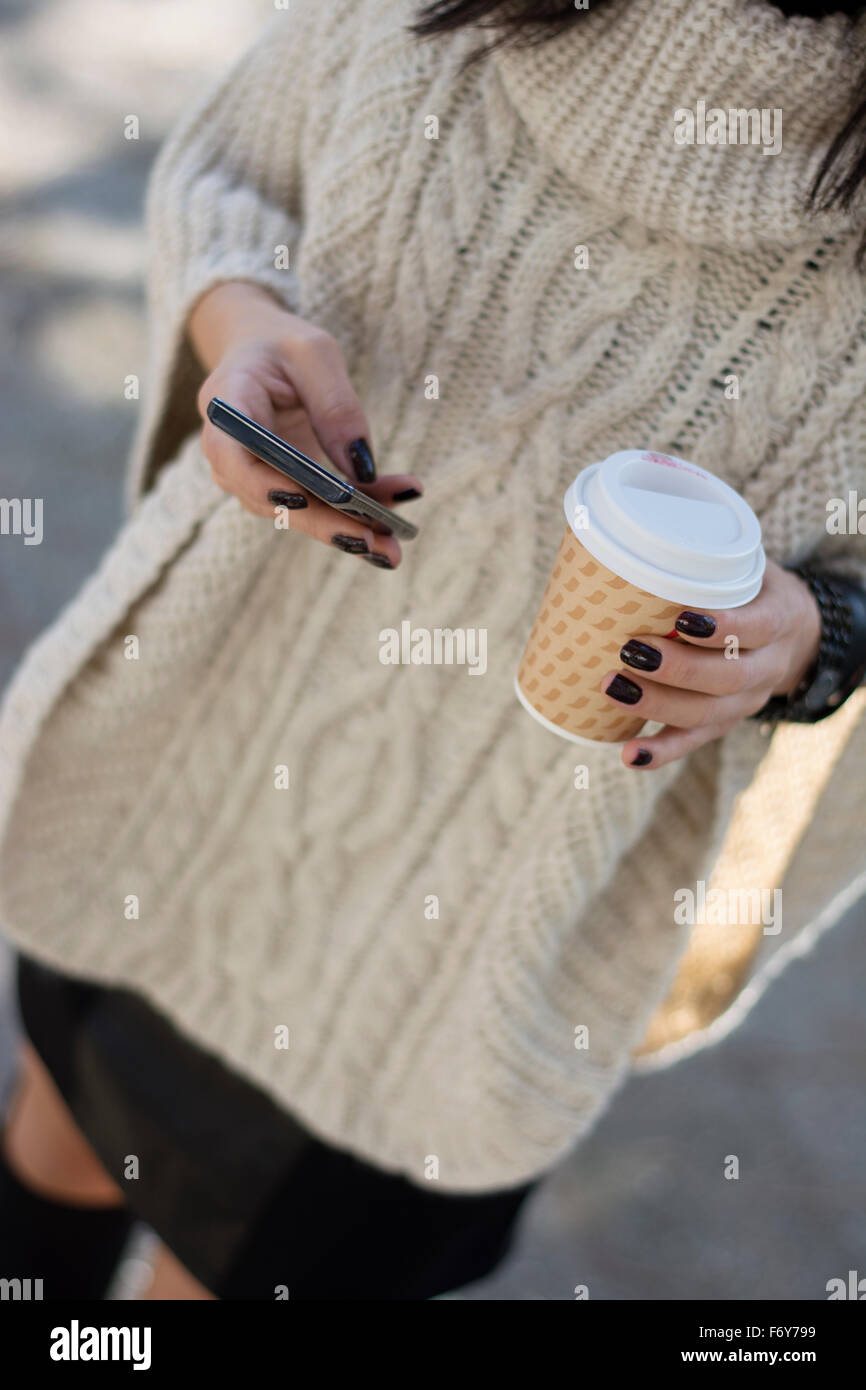Attractive young fashionable woman with black hair using her mobile phone while enjoying fall colors in park Stock Photo
