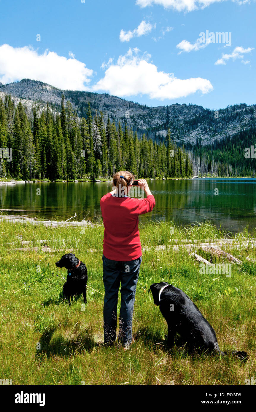 Woman and dogs in the Payette National Forest, Idaho, photographing a mountain lake with a cellphone  (MR No. 01-1915) Stock Photo