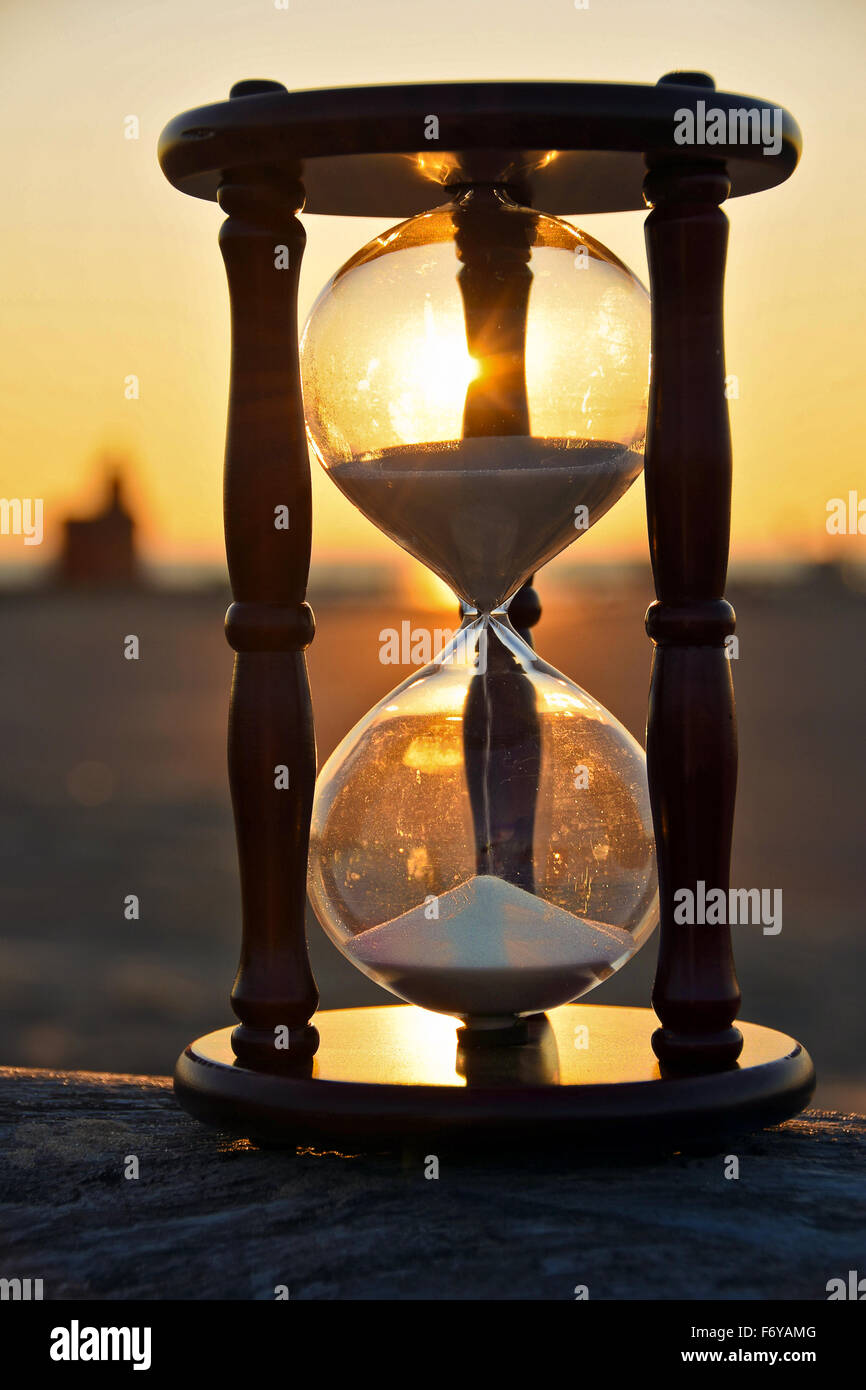 Sand timer on a beach log with sunset background. Stock Photo