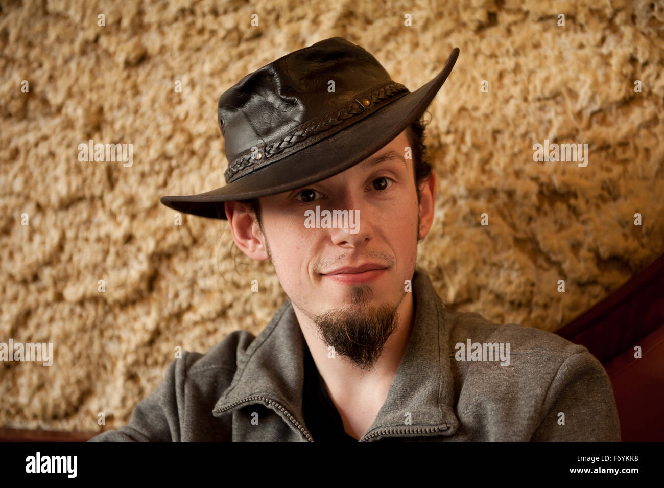 Young man in tip hat portrait, smiling adult European man with small beard sitting in bar in a dark brown Australian theme hat Stock Photo