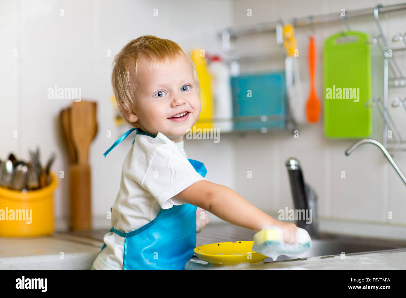 Toddler child washing dishes in kitchen. Little boy having fun with helping to his mother with housework. Stock Photo