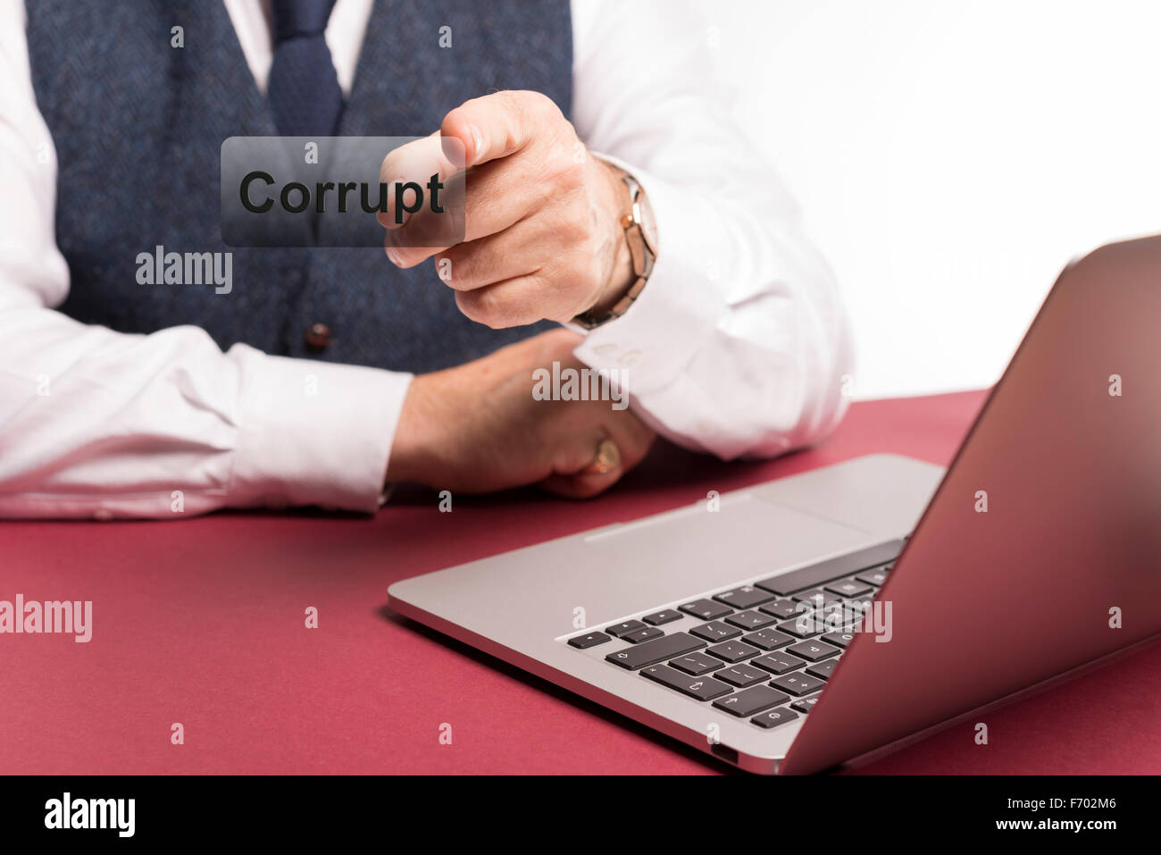 Smartly dressed businessman sitting at office desk with laptop in view pointing at the word corrupt on a clear screen Stock Photo