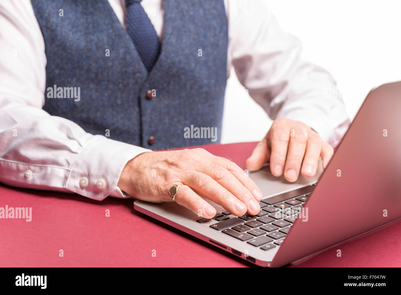 Smartly dressed male sitting at office desk typing on a  laptop  wearing jewelry and a pinkie ring on little finger Stock Photo
