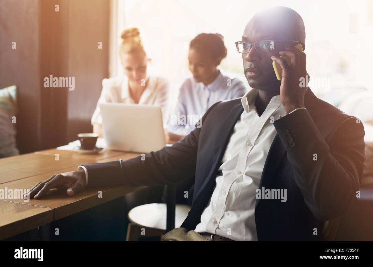 Black business man using cell phone, white and black business woman in background Stock Photo
