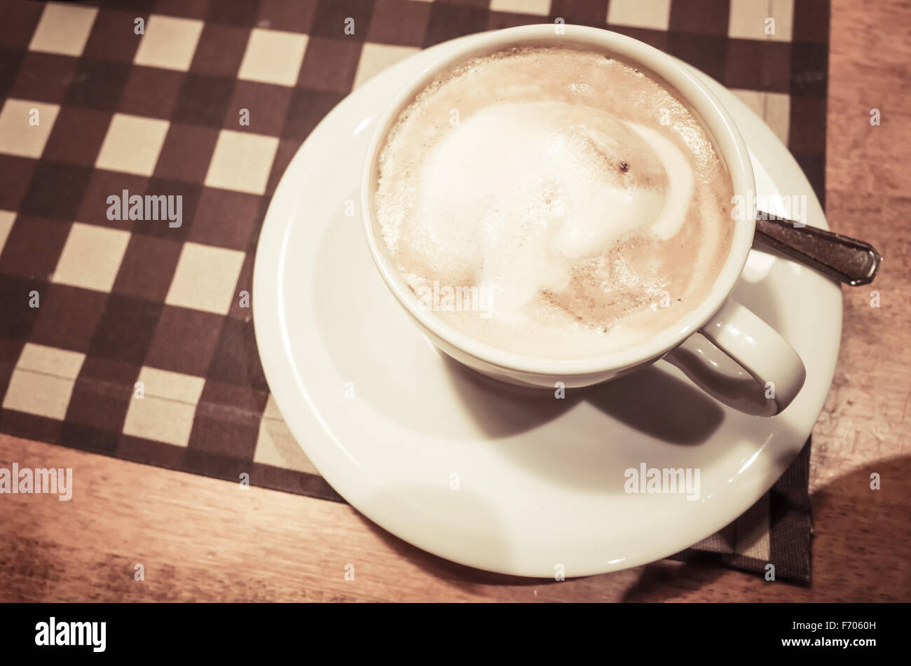 White cup of cappuccino stands on wooden table, retro style warm tonal correction photo filter and selective focus Stock Photo