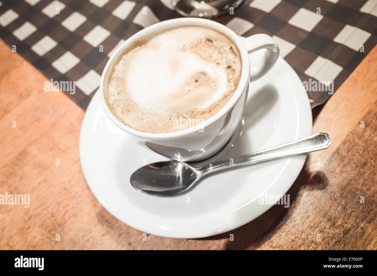 White cup of cappuccino stands on wooden table, retro style tonal correction photo filter and selective focus Stock Photo