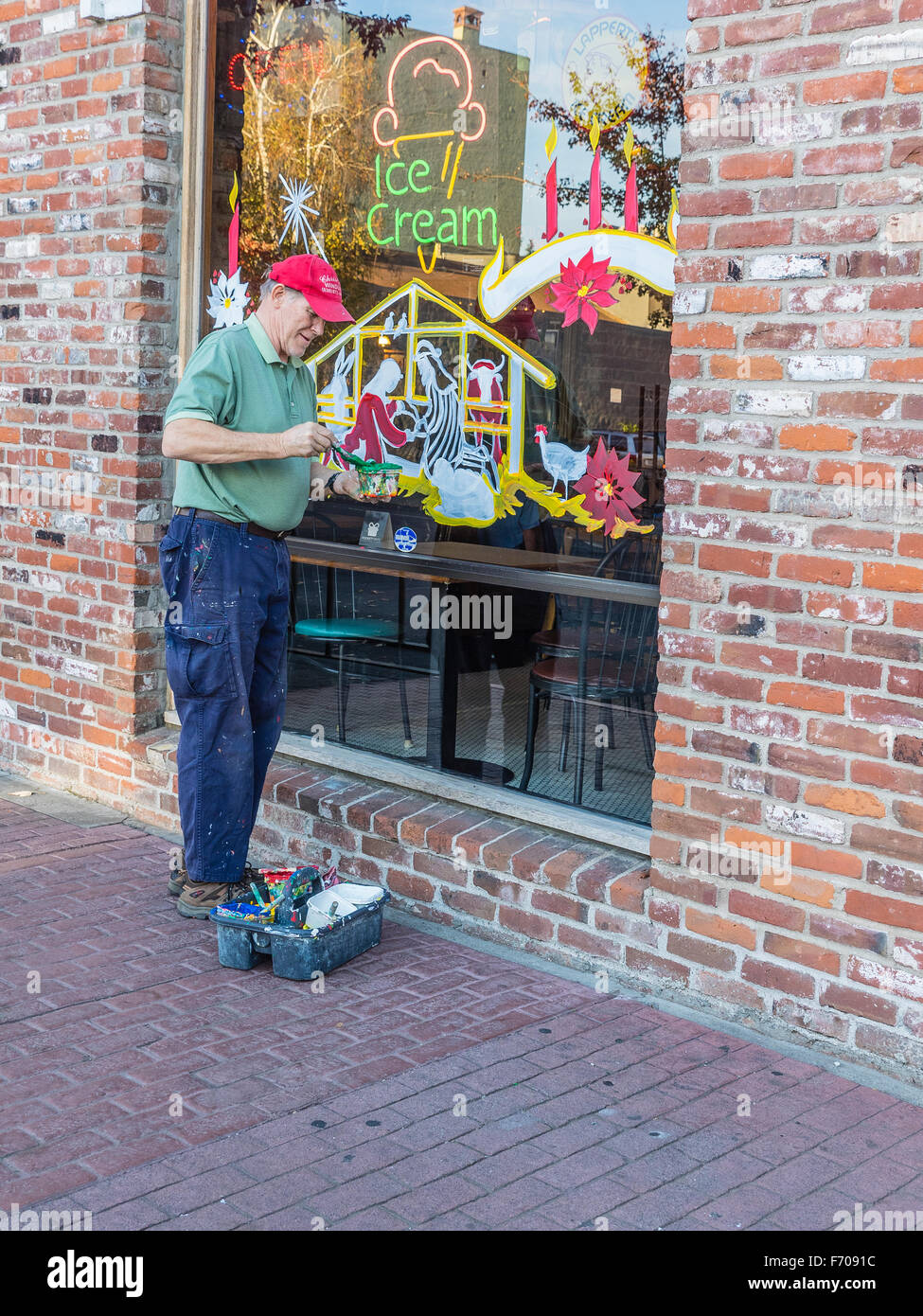 A Christmas window painter stands outside of a store window he is in the process of painting and holds his brush and paint. Stock Photo