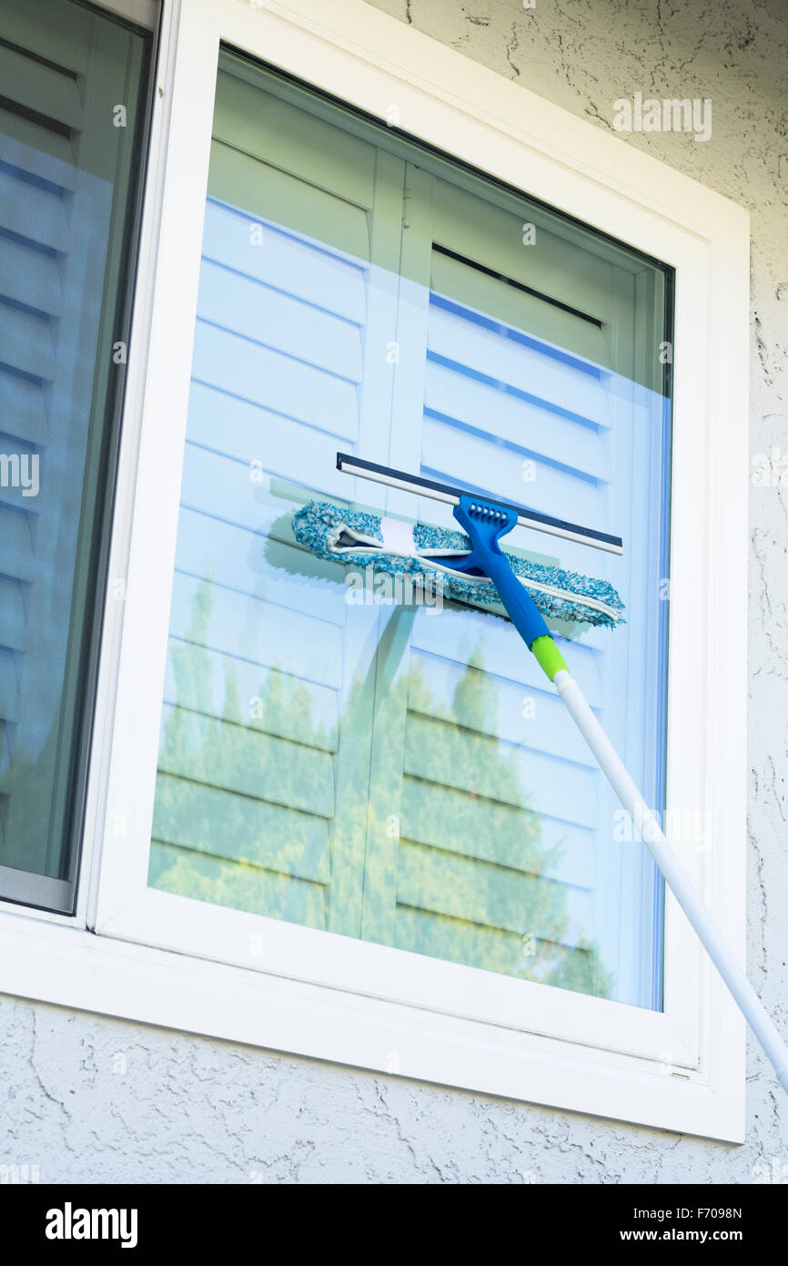 Window washer uses a sponge and squeegee on a pole to wash the exterior windows of a home. Stock Photo