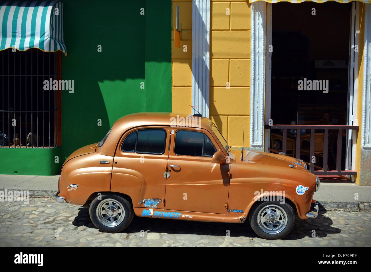 small bronze car parked on a sunny day on a cobbled street next to colourful shops and cafe in Trinidad Cuba Stock Photo