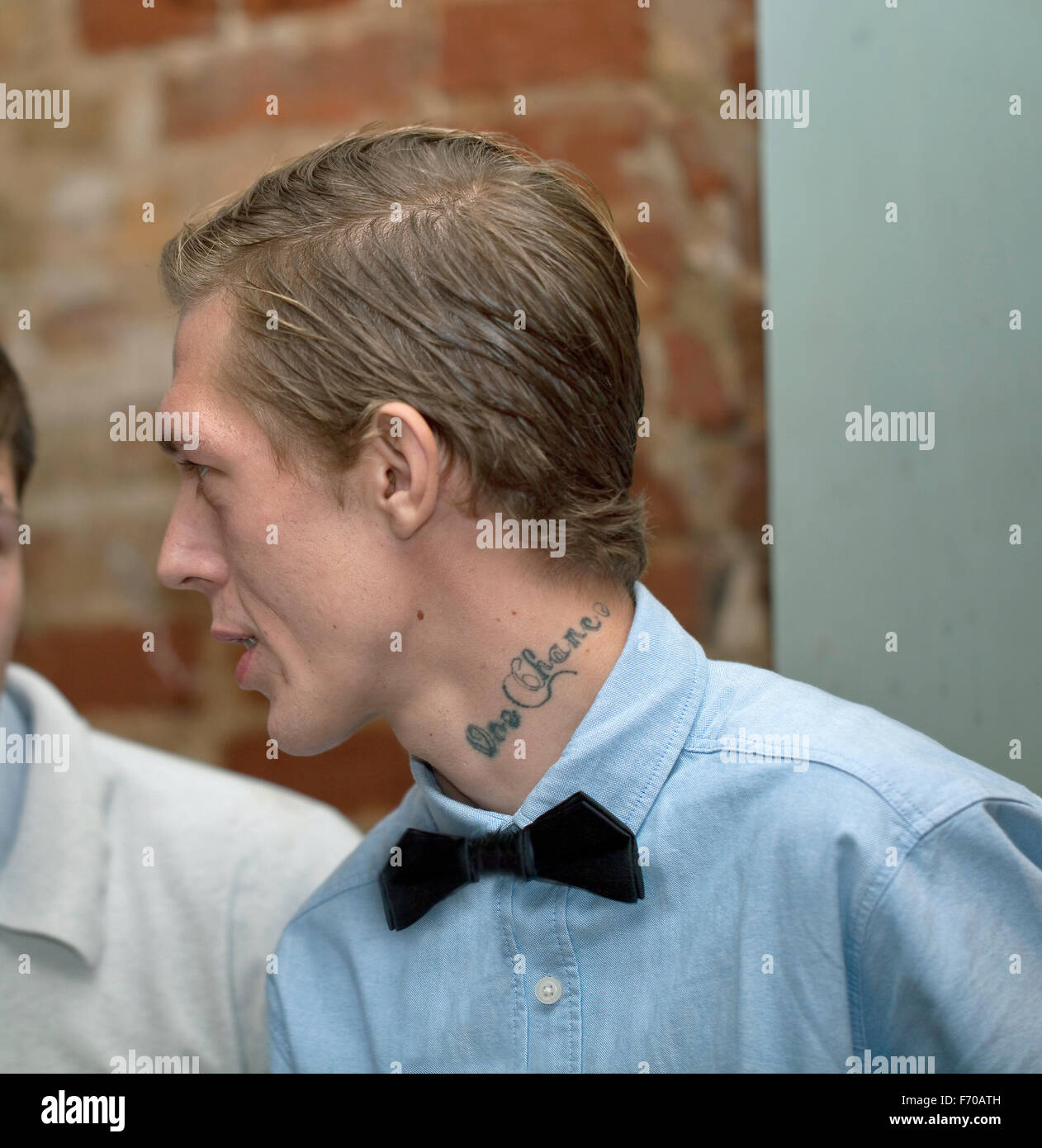 My Bow Tie is Dapper. A young man at his child's christening party shows off his tattoo while chatting to his friend. Stock Photo