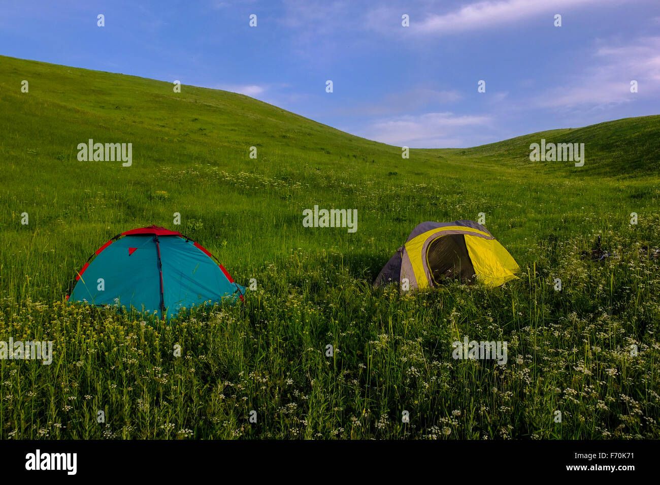 Tents in a lush green field similar to the windows XP wallpaper with a blue sky. Remote adventure camping in beautiful surroundings. Stock Photo