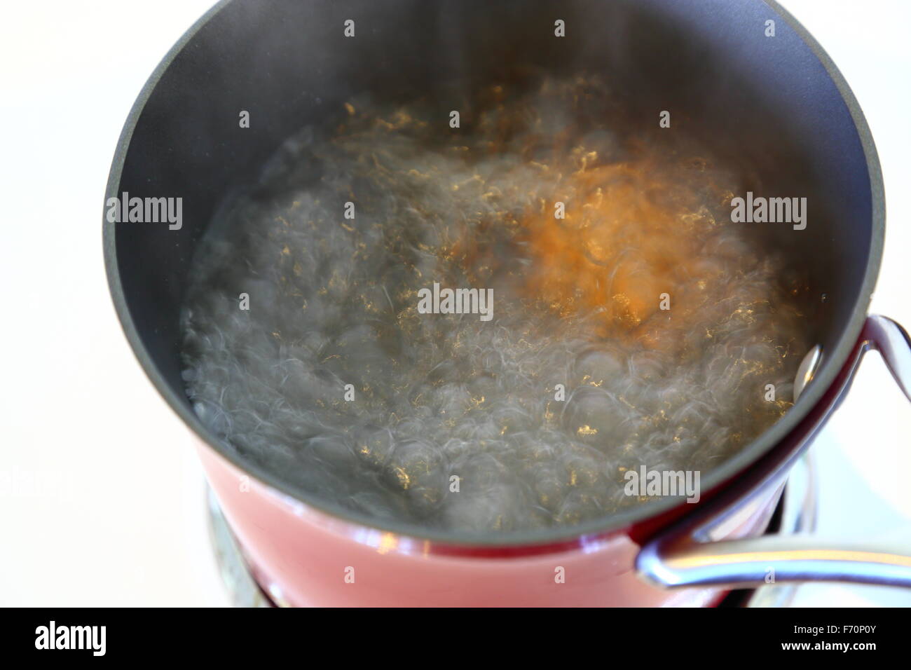 An egg boiling in a red pot on a stove top, viewed from above. Stock Photo
