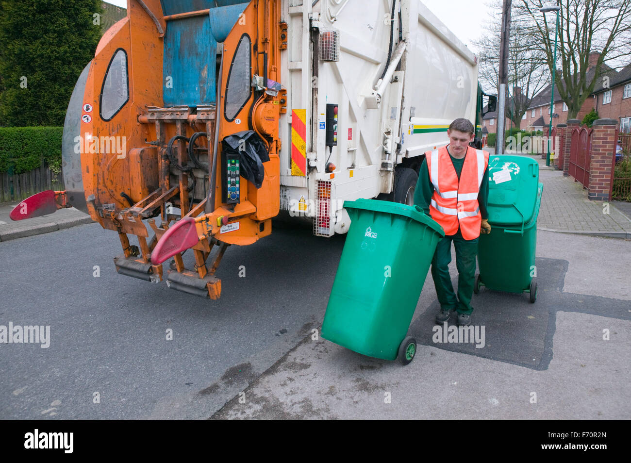 Binman collecting refuse from neighbourhood wheelie bins and loading