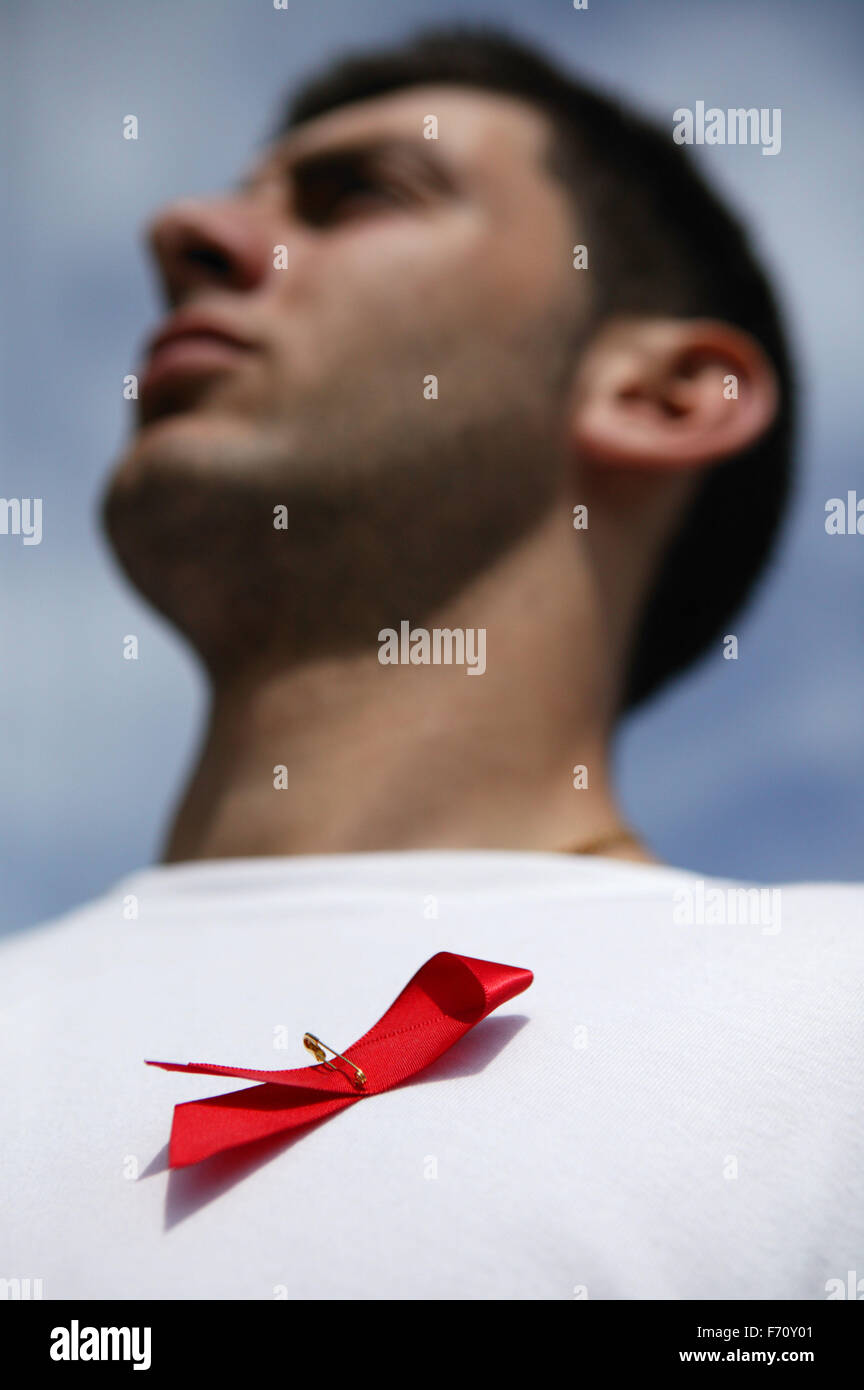 Young man wearing a red bow symbolising World Aids Day sponsored by the HIV and Aids charity; model released for use in HIV and Stock Photo