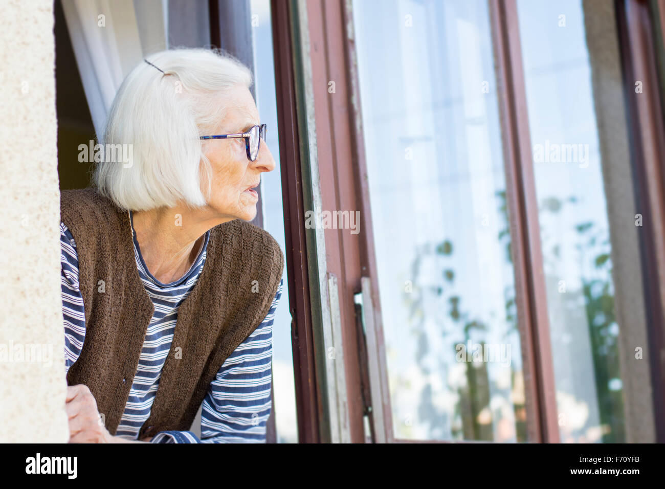 Old and lonely lady looking outside through her window Stock Photo