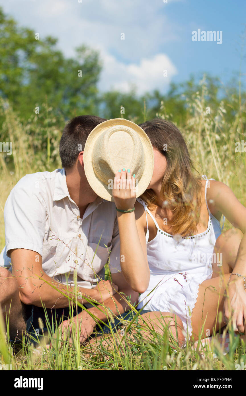Couple kissing in the field behind a straw hat Stock Photo