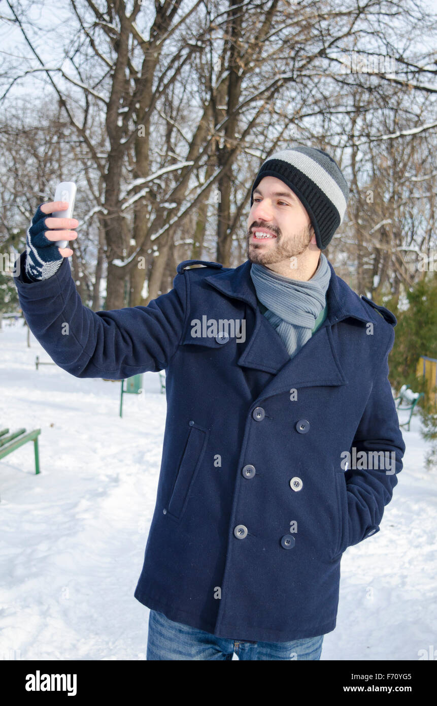 Young bearded man taking a selfie in a park on a sunny winter day Stock Photo