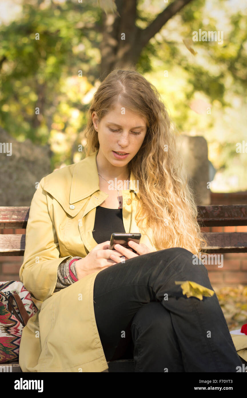 Blonde girl writing text in a park while leaves are falling Stock Photo
