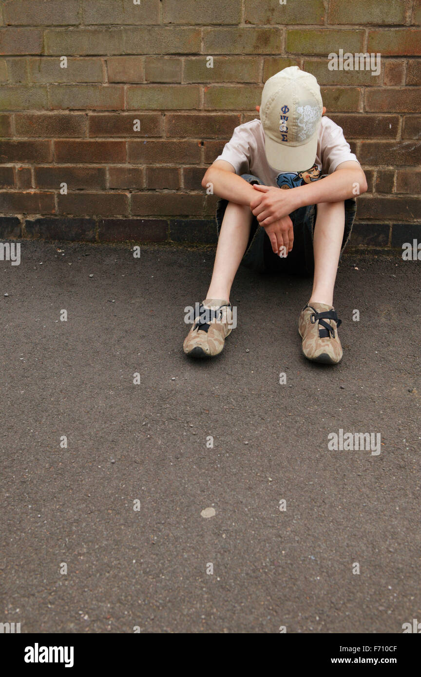Boy sitting by side of wall with his head bowed Stock Photo Alamy