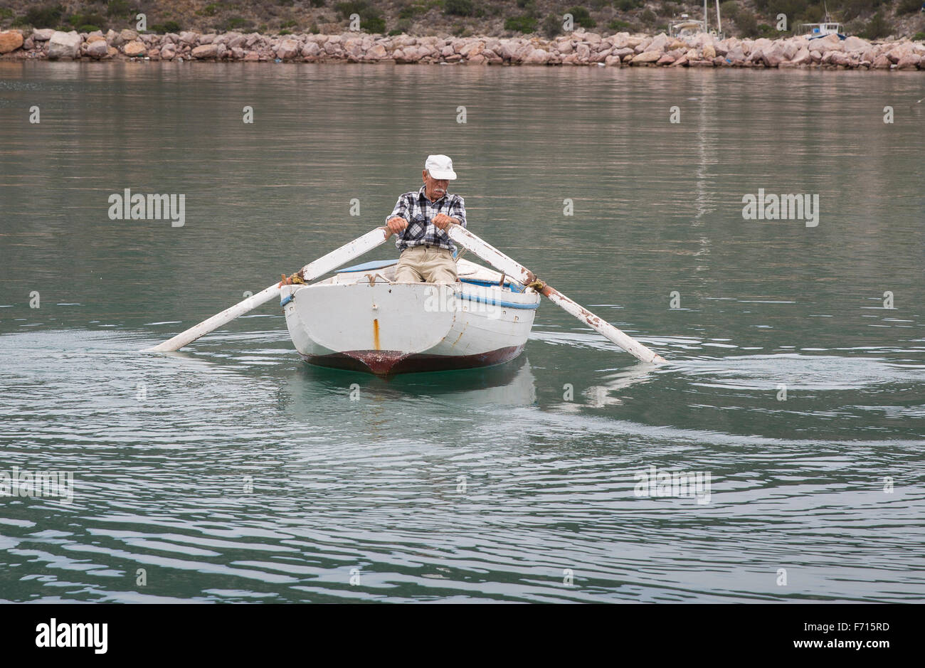 Greek fisherman rowing his boat out of the harbor at Ermioni, Greece and  into the Aegean Sea Stock Photo