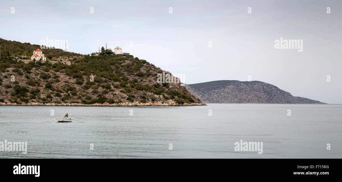 Panoramic scene of a Greek fisherman rowing his boat out of the harbor at Ermioni, Greece and into the Aegean Sea Stock Photo