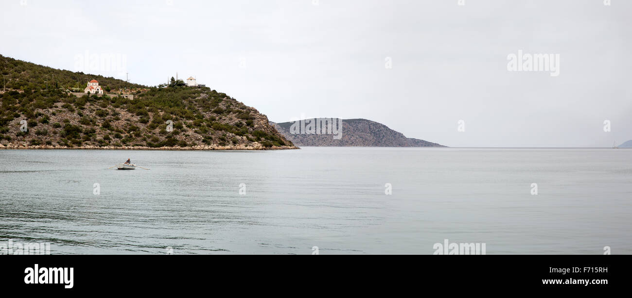 Panoramic scene of a Greek fisherman rowing his boat out of the harbor at Ermioni, Greece and  into the Aegean Sea Stock Photo