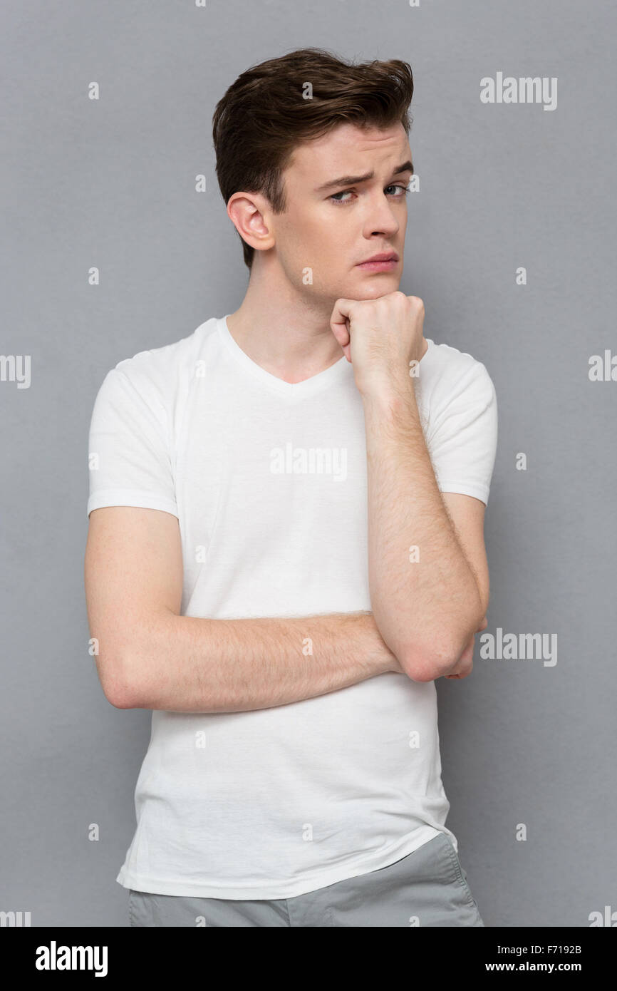 Young handsome attractive thoughtful guy in white t-shirt looking at ...