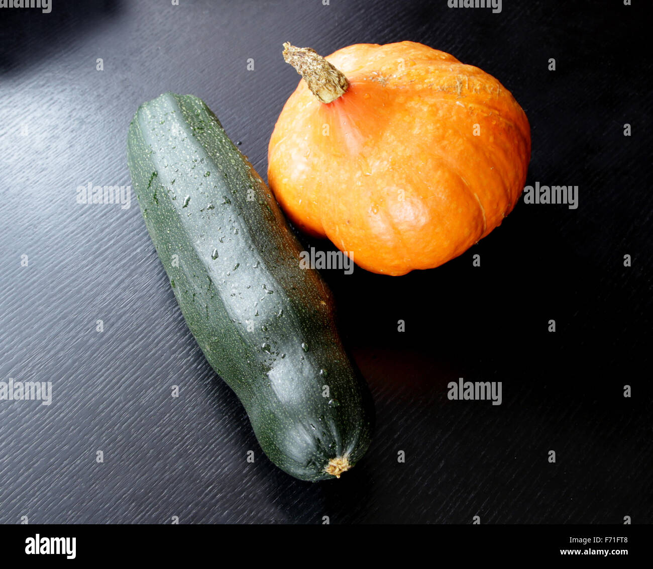 https://c8.alamy.com/comp/F71FT8/orange-pumpkin-and-green-squash-vegetable-marrow-on-black-table-F71FT8.jpg