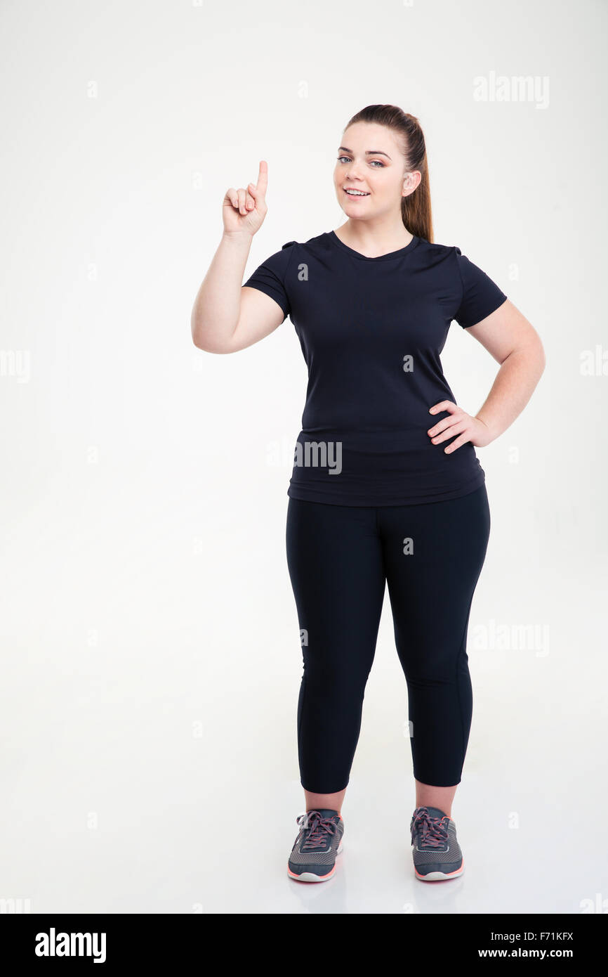 Full length portrait of a happy fat woman in sports wear pointing finger up isolated on a white background Stock Photo