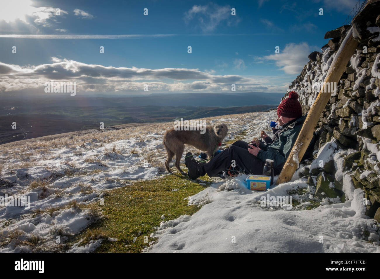 People enjoying snow, sunshine and sandwiches with pet dog at the summit of Penyghent, one of