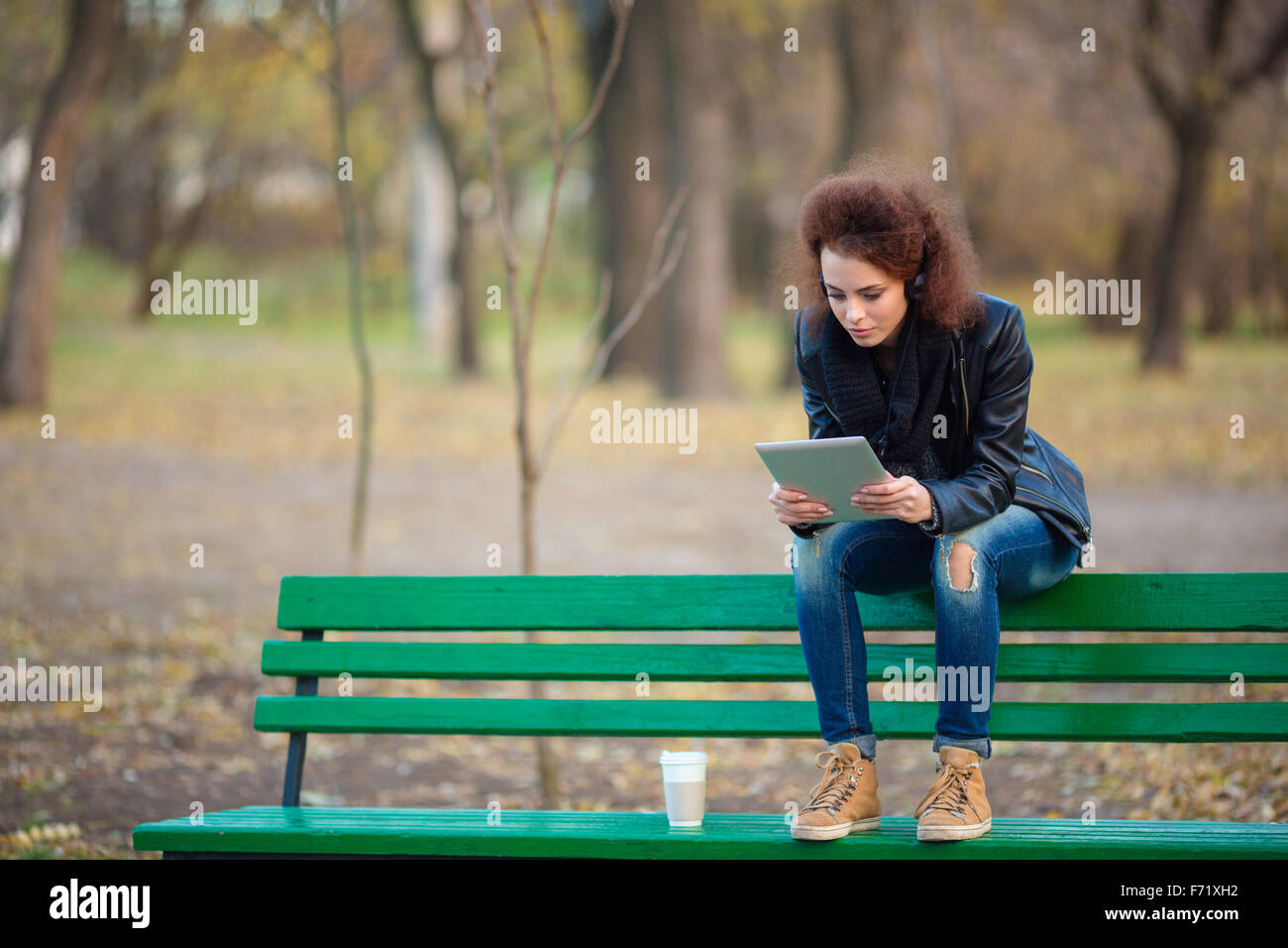 Portrait of a casual woman sitting on the bench and using tablet ...
