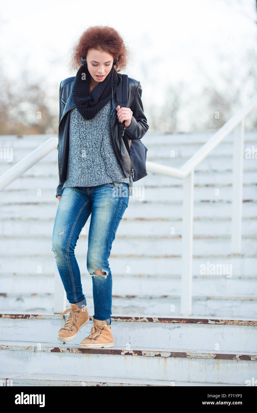 Portrait of a young woman with curly hair walking down stairs outdoors ...