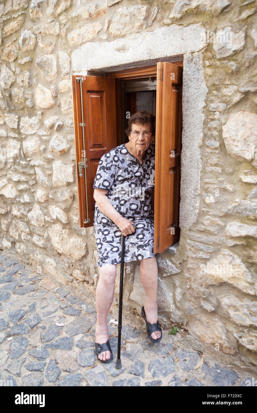 Elderly woman sitting on a window sill outside a house in the village of Mesta, Chios, Greece Stock Photo