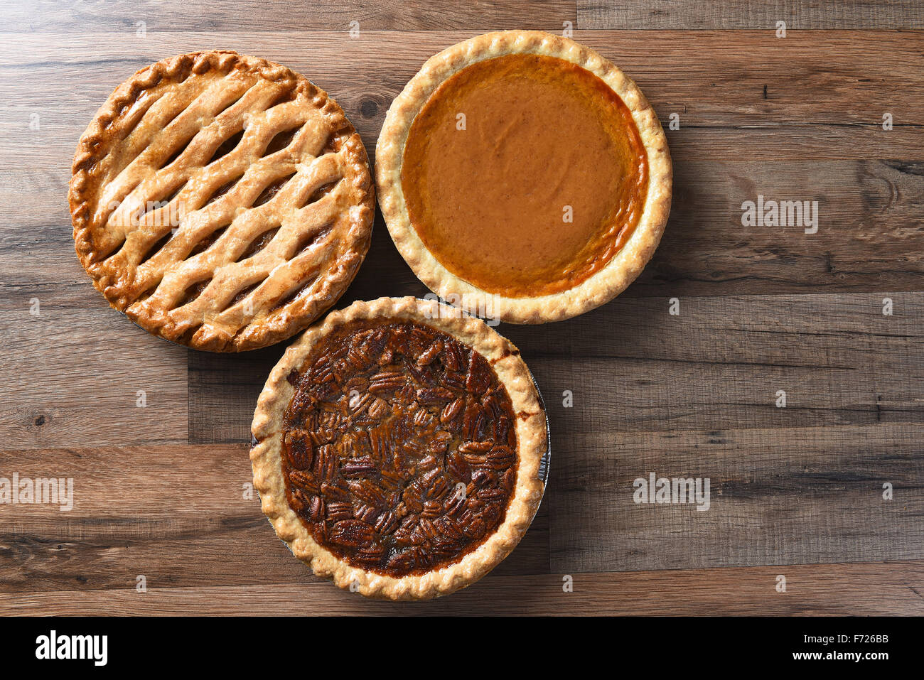 Three pies for Thanksgiving on a wood surface. The desserts include apple, pumpkin and pecan pies - all traditional treats for t Stock Photo