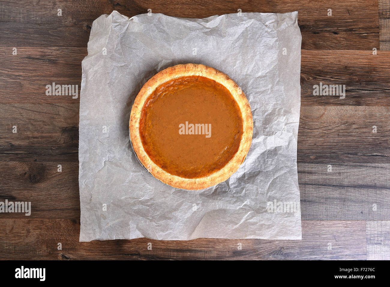 Overhead view of a whole pumpkin pie on parchment paper and dark wood table. Stock Photo