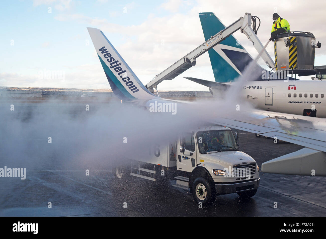 Airport ground crew spraying deicing fluid on Westjet Boeing 737 plane wing to remove ice and snow prior to takeoff in winter Stock Photo
