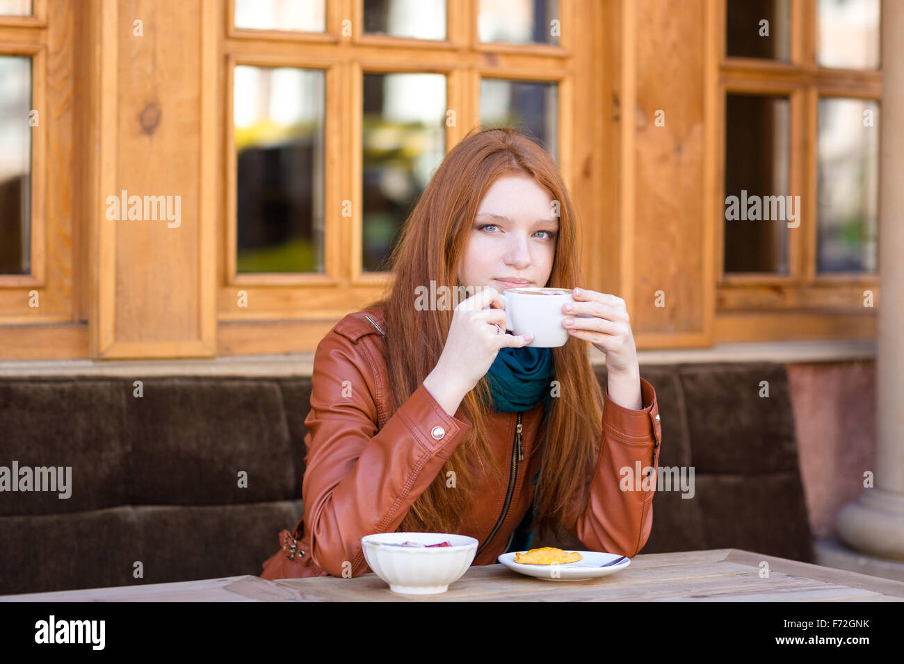 Pensive woman with beautiful long red hair sitting with coffee cup  and dreaming in outdoor cafe Stock Photo