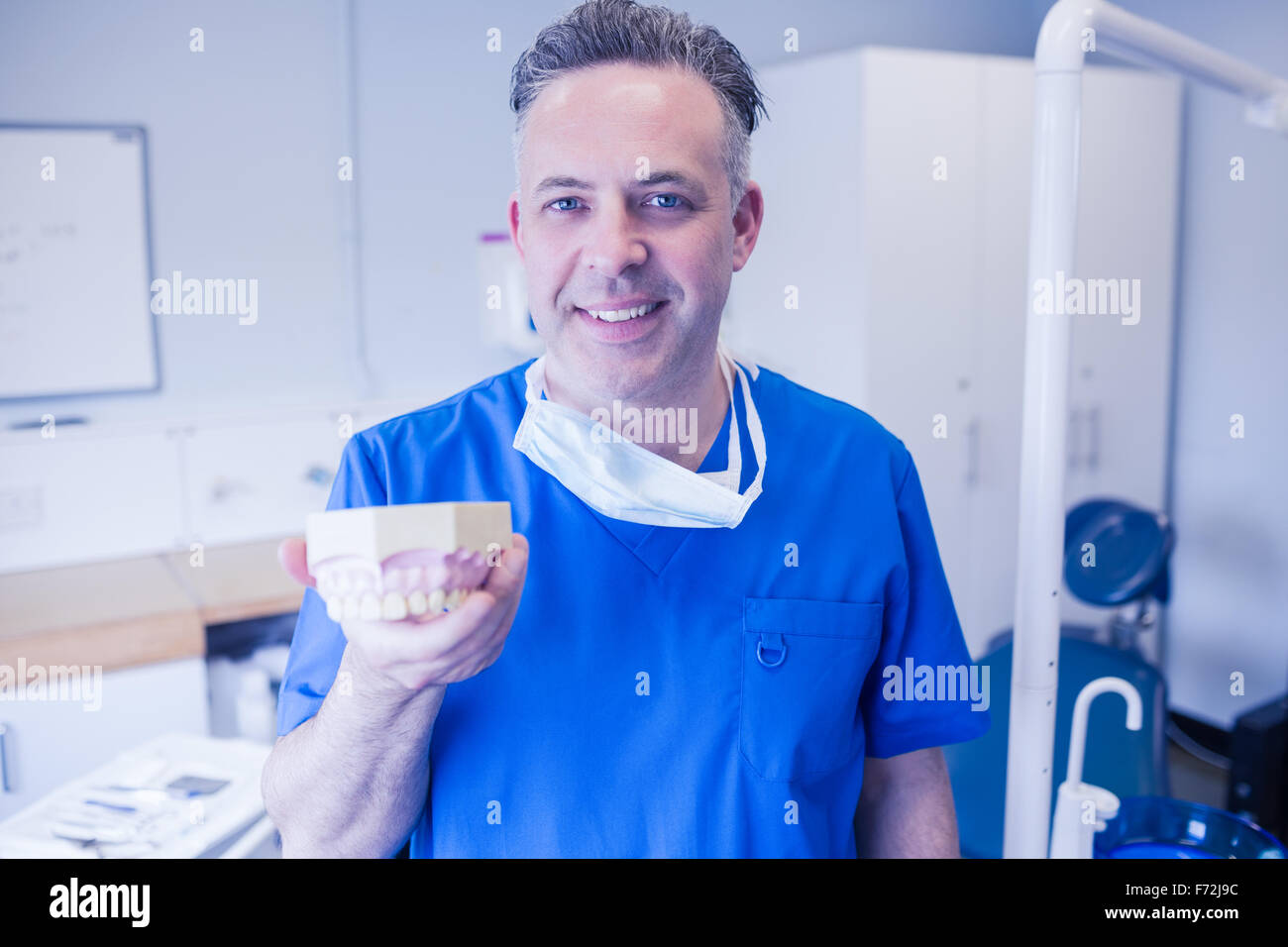 Dentist in blue scrubs holding mouth model Stock Photo Alamy