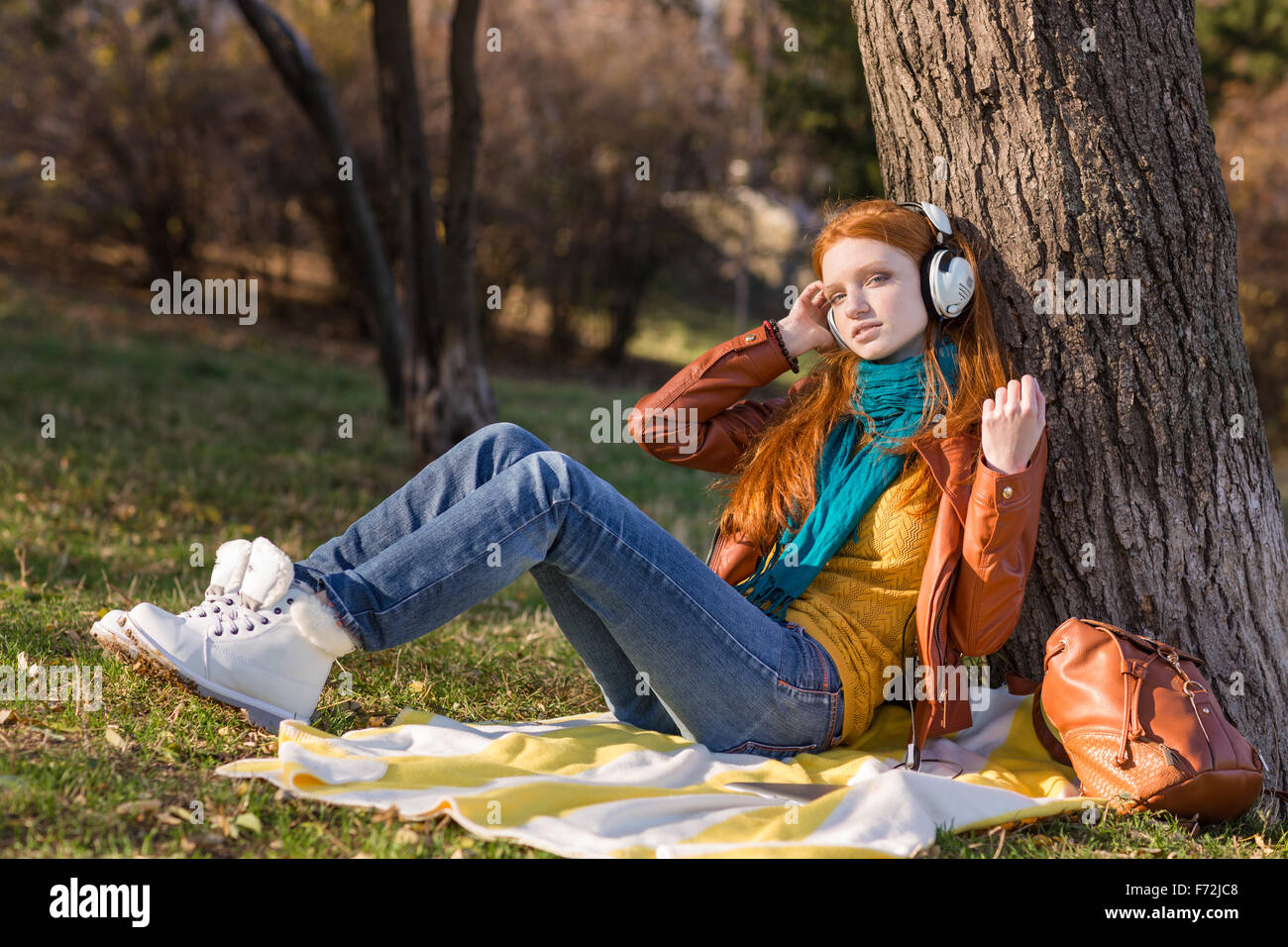 Attractive relaxed young lady listening to music sitting under the tree in the park Stock Photo