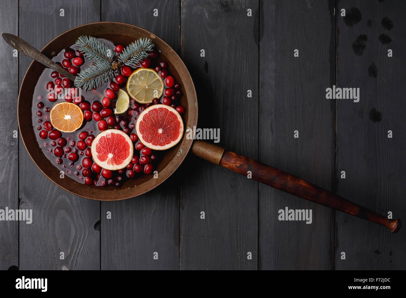 Hot winter punch,sangria,toddy or mulled wine with lemon, grapefruit,tangerine, lime and cranberry in aged rustic brass pot over Stock Photo