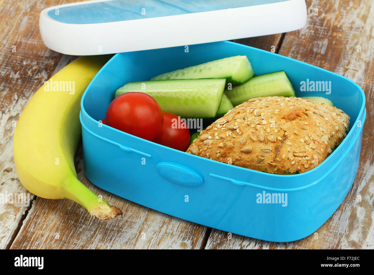 Healthy lunch box consisting mixed grain cheese roll, cherry tomatoes, cucumber sticks and banana Stock Photo