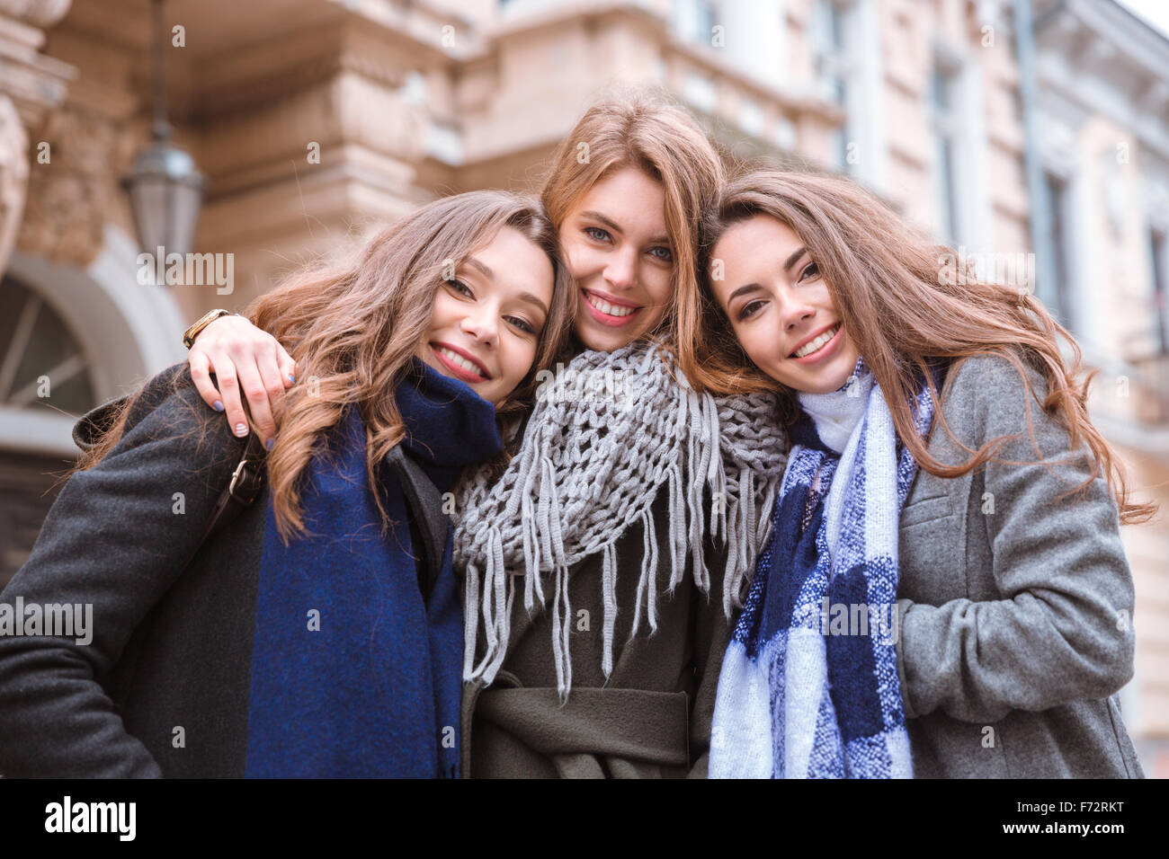 Portrait of a three smiling girlfriends standing together outdoors with ...