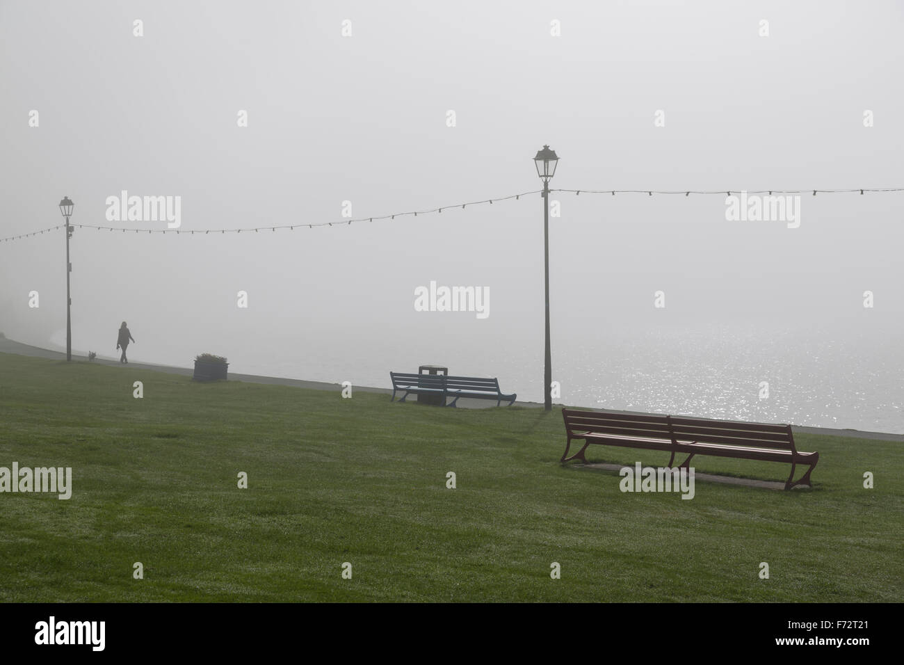 Woman walking with a dog in fog on a seaside promenade, UK Stock Photo