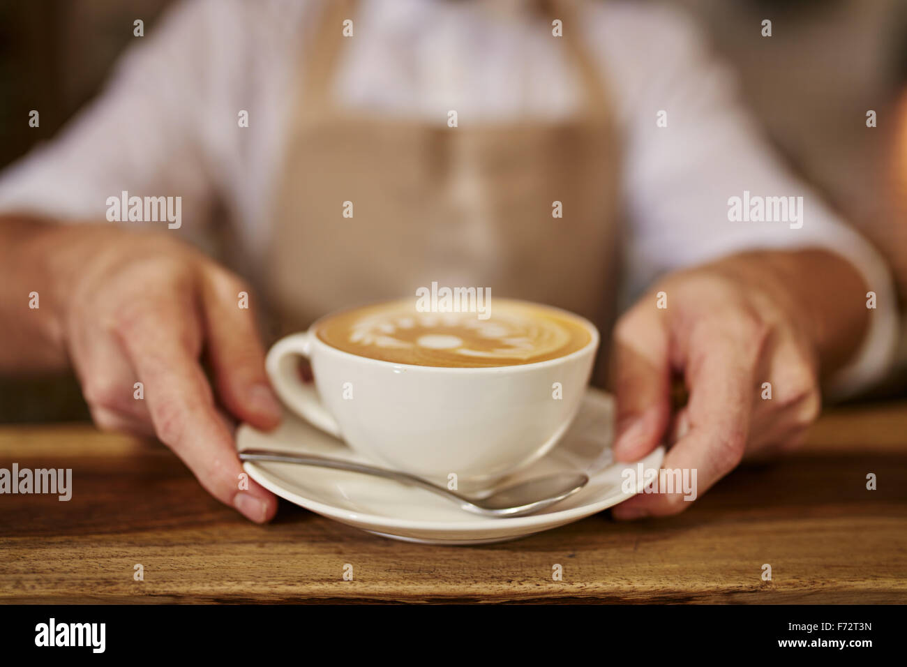 Close up of man serving coffee while standing in coffee shop. Focus on male hands placing a cup of coffee on counter. Stock Photo