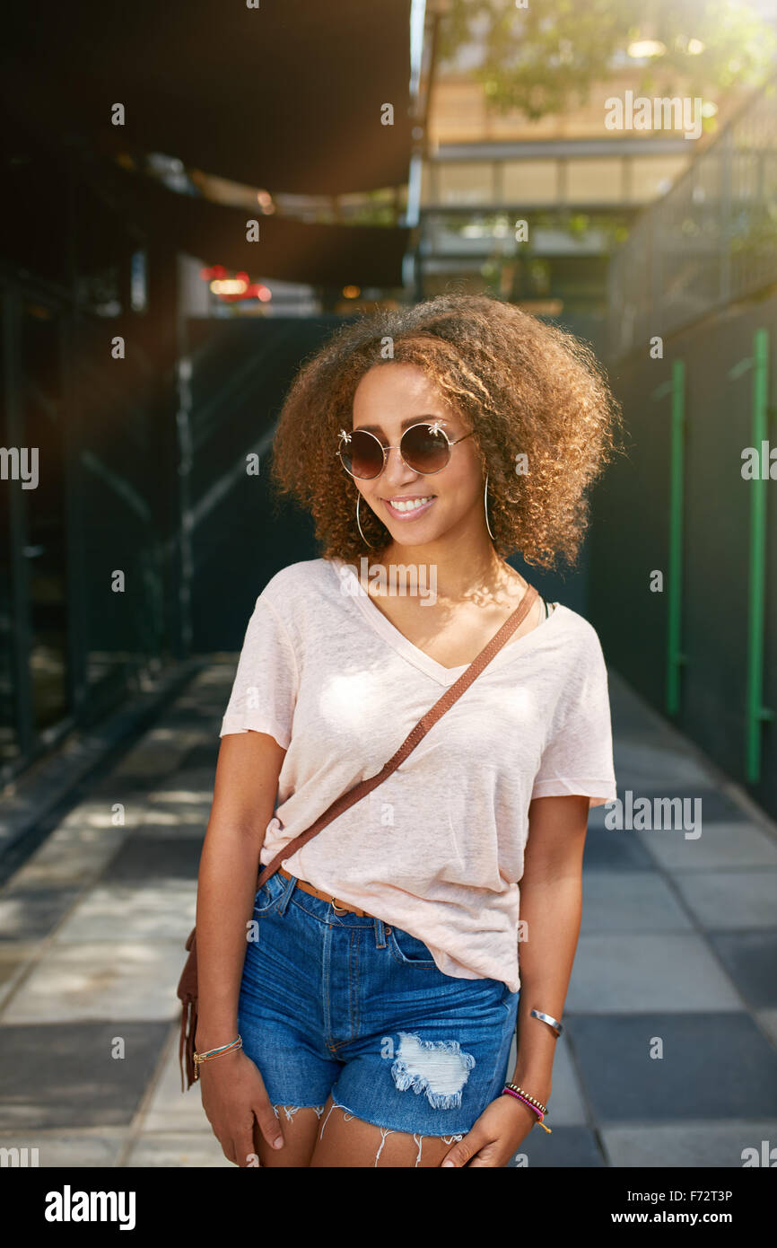 Portrait of a beautiful young black woman wearing sunglasses smiling at camera. African young female in casuals posing outdoors. Stock Photo