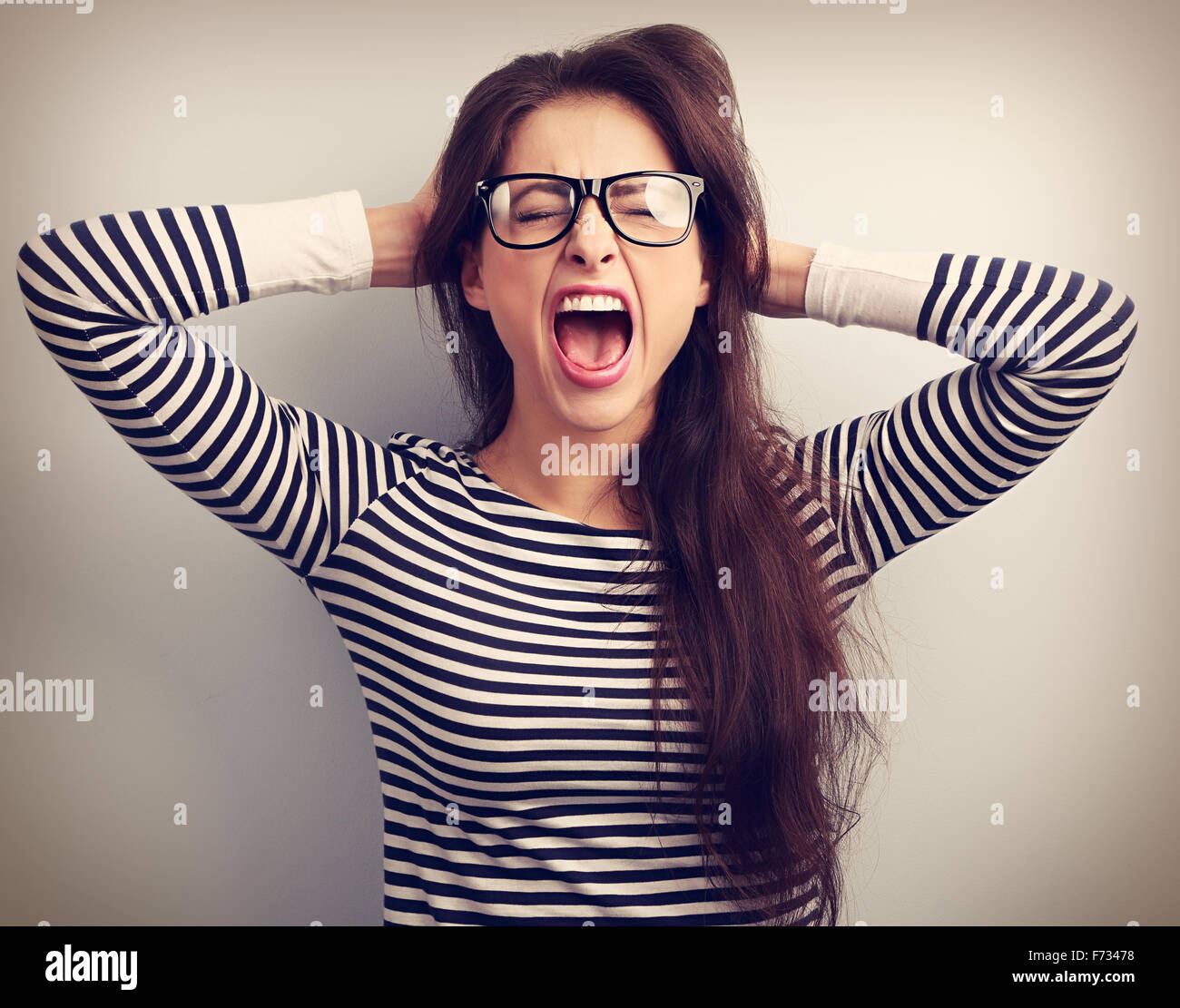 Angry young business woman in glasses strong screaming with wild open mouth and holding head the hands. Toned closeup portrait Stock Photo