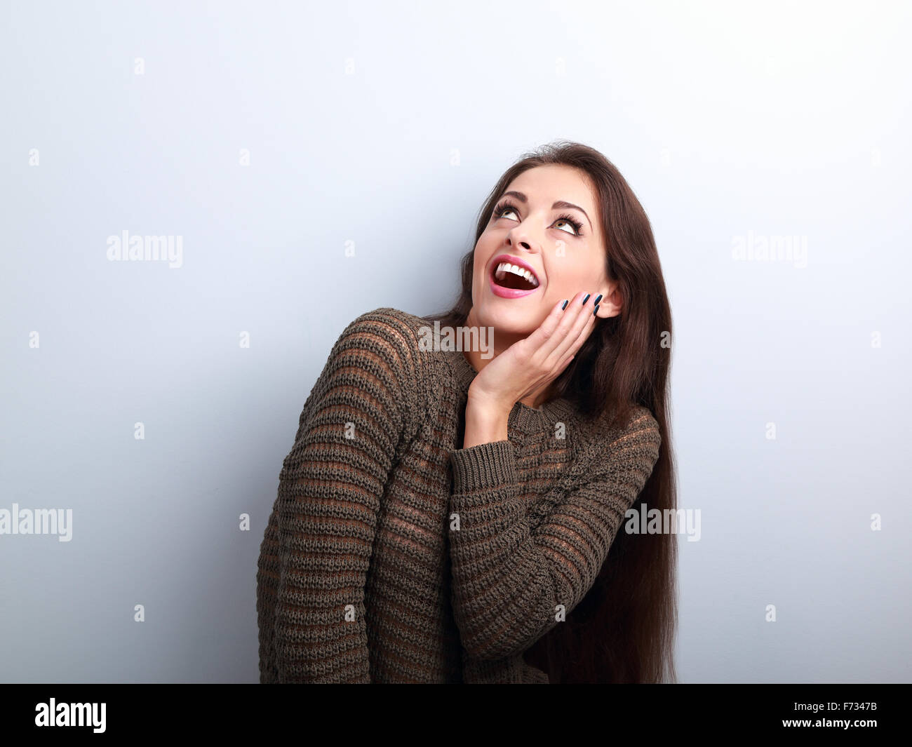 Excited surprising young woman with open mouth looking up on blue background Stock Photo