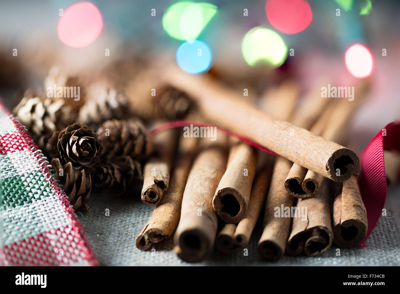 Cinnamon sticks close up with small pine cones and festive holiday lights in the background Stock Photo