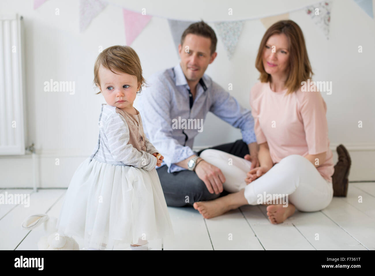 Couple with their young daughter sitting on the floor in photographers studio, posing for a picture. Stock Photo